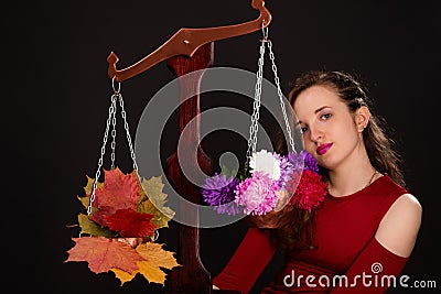 A saleswoman of beautiful autumn mood weighs flowers and colorful autumn maple leaves on a scales. Funny concept Stock Photo