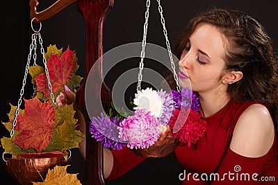 Saleswoman of beautiful autumn mood weighs flowers and colorful autumn maple leaves on scales. Funny concept Stock Photo