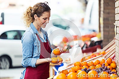 Saleswoman selecting fresh fruit and preparing for working day in health grocery shop. Stock Photo