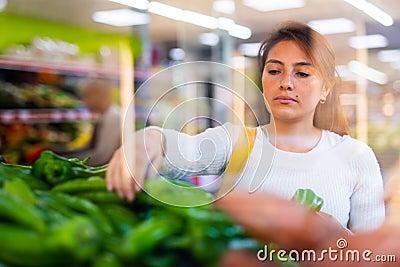 Spanish woman employee in vegetable store with green peppers Stock Photo