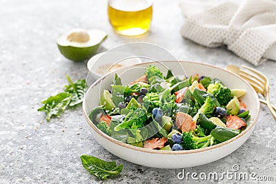 Salmon fish and avocado salad with fresh spinach leaves, broccoli, blueberry dressed with olive oil Stock Photo