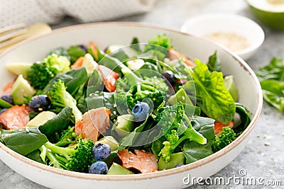 Salmon fish and avocado salad with fresh spinach leaves, broccoli, blueberry dressed with olive oil Stock Photo