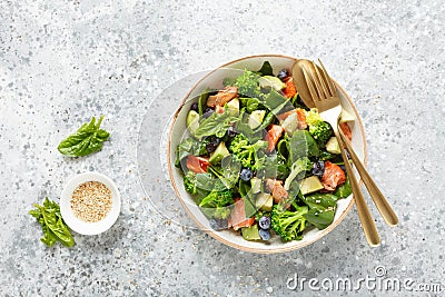 Salmon fish and avocado salad with fresh spinach leaves, broccoli, blueberry dressed with olive oil Stock Photo