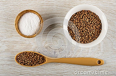 Salt in bamboo bowl, buckwheat in white bowl, spoon with raw buckwheat on table. Top view Stock Photo