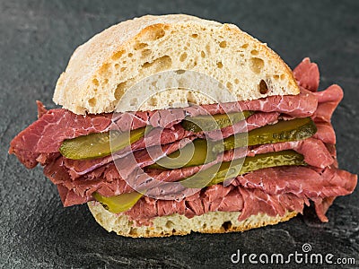 Salt Beef or Pastrami Cold Meat With Gherkins in a Ciabatta Bread Roll or Stock Photo