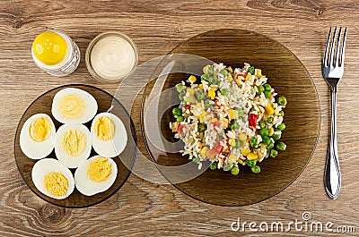 Salt, bowl with mayonnaise, saucer with halves boiled eggs, plate with vegetable mix, fork on table. Top view Stock Photo