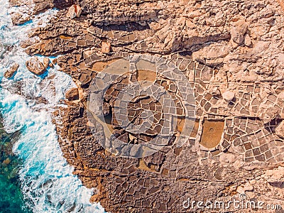 Salt farms in rocks of coast, ancient way of evaporation sea water by sun. Aerial top view. Stock Photo