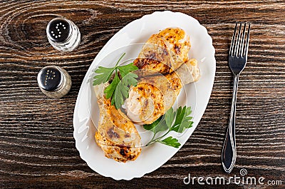 Salt and pepper, grilled chicken legs, leaves of parsley in dish, fork on table. Top view Stock Photo