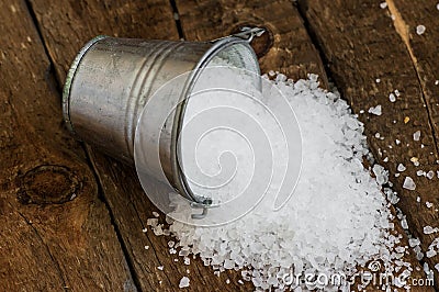 Salt spill out of the bucket tin on a wooden board Stock Photo