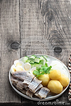Salted herring with boiled potatoes and quial eggs on a white plate on wooden table Stock Photo