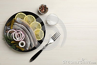 Salted herring fillets served with onion rings, pickles, dill and lemon on light beige wooden table, flat lay. Space for text Stock Photo