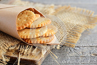 Salty thin crackers in a wrapping paper and on a sackcloth. Vintage wooden background. Tasty crispy crackers snack idea Stock Photo