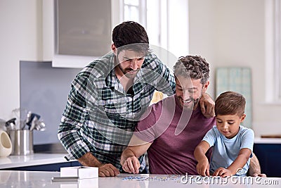 Same Sex Family With Two Dads And Son Doing Jigsaw Puzzle In Kitchen At Home Stock Photo