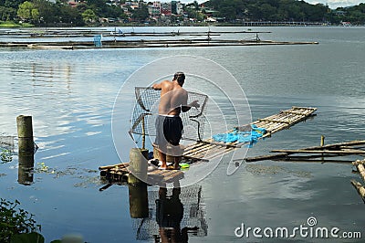 Massive Man launching fish trap snare on lake water Editorial Stock Photo