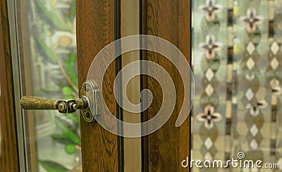 Sample of modern wooden window profile on sill indoors. Door hand in retro style. Behind the glass, abstract stained-glass windows Stock Photo