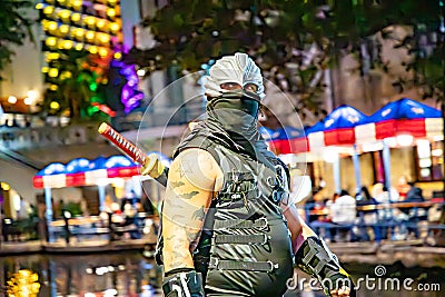 people at Halloween walk along the San Antonio River Walk with costumes by night with illuminated trees and restaurants Editorial Stock Photo