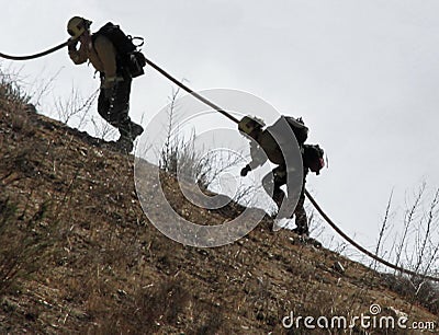 Firemen with hose climbing hill Editorial Stock Photo