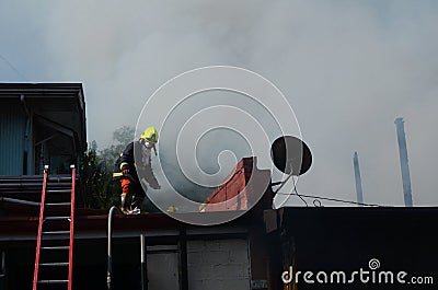 Lone fireman on top of the roof walking away from thick smoke from burning house Editorial Stock Photo