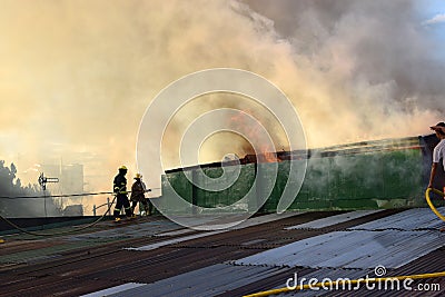 Firemen and volunteers on rooftop put out fire using fire hose during house fire that gutted interior shanty houses Editorial Stock Photo