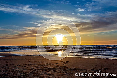 Sand beach with endless horizon and foamy waves under the bright sundown with yellow colors and clouds above the sea Stock Photo