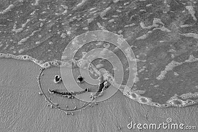 On the sand drawn a smiley face and a wave washes, black and white Stock Photo