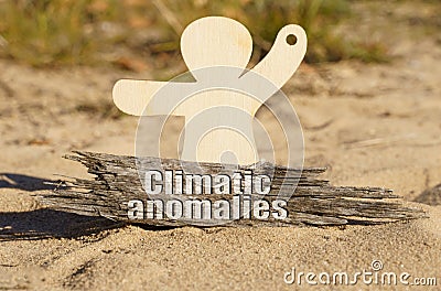 On the sand near the wooden figurine of a man there is a piece of wood with the inscription - Climatic anomalies Stock Photo