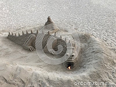 A sand sculpture in the shape of a dragon that exhales fire from the mouth located on the beach Stock Photo