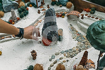 Sand therapy. Man arranges with his hand toy miniature trees and small houses in a sand box. Stock Photo