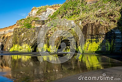 Sandstone cliff formation reflecting in the water at the Three Sisters beach on the Tasman Sea shores of Taranaki, New Zealand Stock Photo