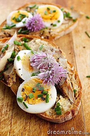 Sandwich with adition of mackerel fish , eggs and edible flowers of chives on wooden table Stock Photo