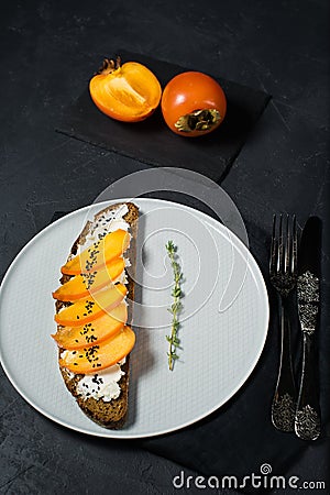 Sandwich with persimmon and soft cheese on a black background. Stock Photo
