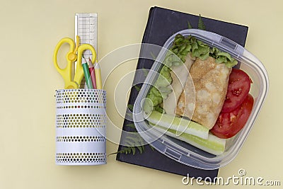 Sandwich with vegetables in a container, school lunch, multicolored pencils and book on a yellow background, top view Stock Photo