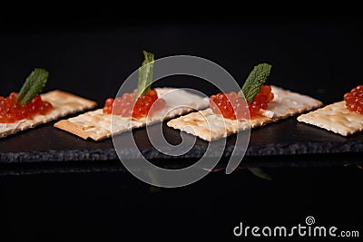 Sandwiches of cracker canapes with red caviar and butter and a leaf of green mint on a plate of slate. Seafood, red caviar. Stock Photo