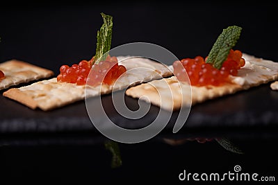 Sandwiches of cracker canapes with red caviar and butter and a leaf of green mint on a plate of slate. Seafood, red caviar. Stock Photo