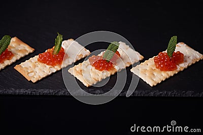Sandwiches of cracker canapes with red caviar and butter and a leaf of green mint on a plate of slate. Seafood, red caviar. Stock Photo