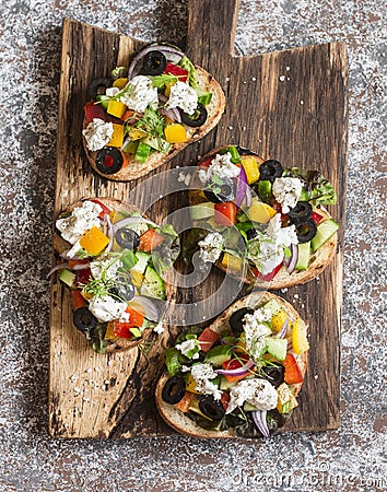 Sandwiches with feta, tomatoes, cucumbers and olives. Greek salad bruschetta style on a rustic cutting board. Stock Photo