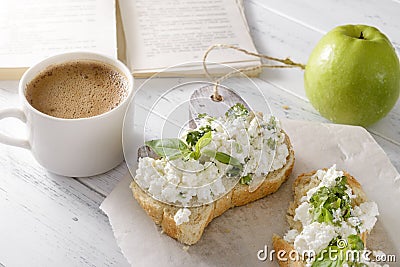 Sandwiches with soft cheese and Basil on a plate, a Cup of hot black coffee, a green Apple, a book on a white table, a delicious Stock Photo