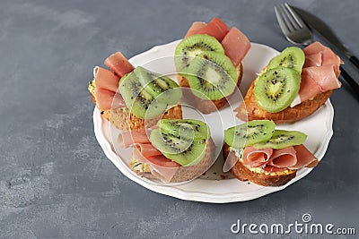 Sandwiches with soft cheese, jamon and kiwi on a white plate. Delicious and healthy breakfast Stock Photo