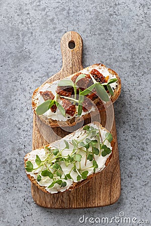 Sandwiches on toast with sun-dried tomatoes, fresh radish microgreens, cream cheese on grey . Top view. Vertical format Stock Photo