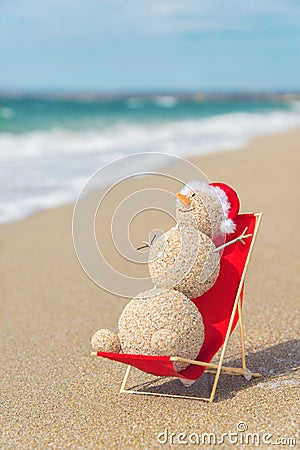 Sandy snowman in santa hat sunbathing in beach lounge. Stock Photo