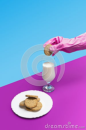 Sanitary pink glove holding a sweet cookie above a glass of milk on a pastel pink and blue background Stock Photo