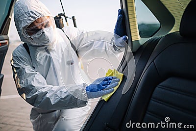 Sanitizing service worker cleans the car`s interior with a yellow rug. A man in a protective suit, mask and gloves disinfects the Stock Photo