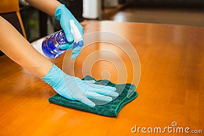Sanitizing surfaces cleaning kitchen table with disinfectant spray bottle with towel and gloves. COVID-19 prevention. Stock Photo