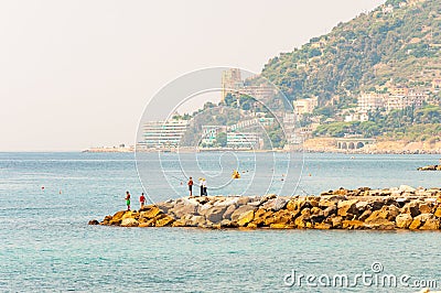 Fishing fishermen standing on rocky marina on Sanremo riviera Liguraian Sea coast with landscaped highland cityscape on the Editorial Stock Photo