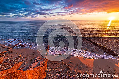 Sanremo, Riviera dei Fiori, Liguria, Italy. Scenis rocks and pebbles on beach illuminated beautiful by sunset light. Dramatic Stock Photo