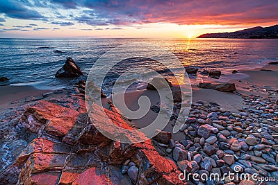 Sanremo, Riviera dei Fiori, Liguria, Italy. Scenis rocks and pebbles on beach illuminated beautiful by sunset light. Dramatic Stock Photo