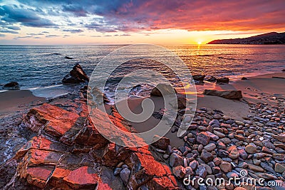 Sanremo, Riviera dei Fiori, Liguria, Italy. Scenis rocks and pebbles on beach illuminated beautiful by sunset light. Dramatic Stock Photo