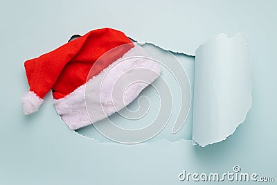 Santa Claus Christmas hat in a big torn pastel blue paper hole. Minimalism. New Year concept. Flat lay. Horizontal frame Stock Photo