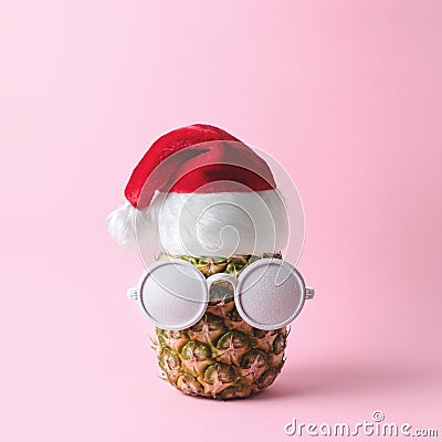 Santa Claus face made from pineapple and white painted sunglasses on pink background. Stock Photo