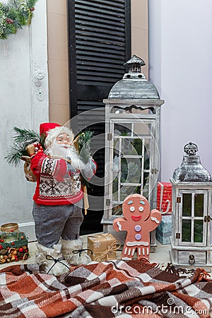 Santa Claus and gingerbread man toys standing on brown plaid with decorative lanterns and Christmas presents. Stock Photo